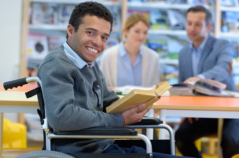 Rapaz cadeirante com livro sorrindo
