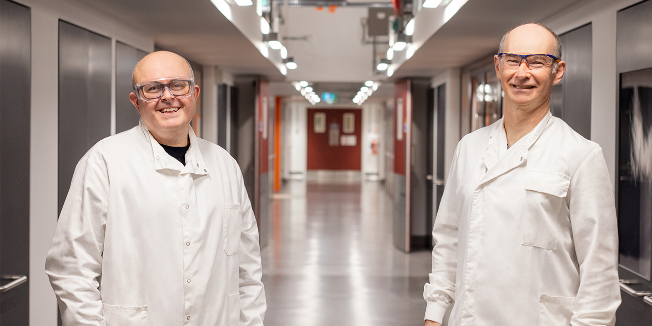 Dois cientistas sorrindo em um corredor, educação médica independente.
