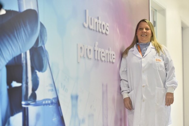 Colaboradora posando para uma foto no ambiente de trabalho com um banner ao fundo